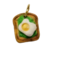 A small food-themed charm or pendant featuring a slice of toast with a fried egg and green leaves, centered on a plain white background.